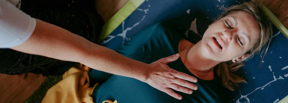Trainerin begleitet eine liegende Frau mit einer Hand auf der Brust
