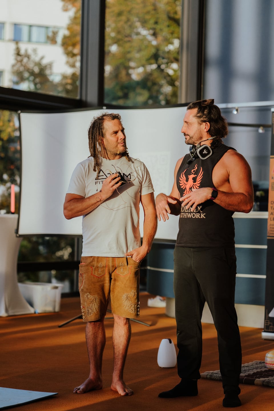 Fetzy und James stehen mit Mikrofon und Kopfhörern vor einer Leinwand