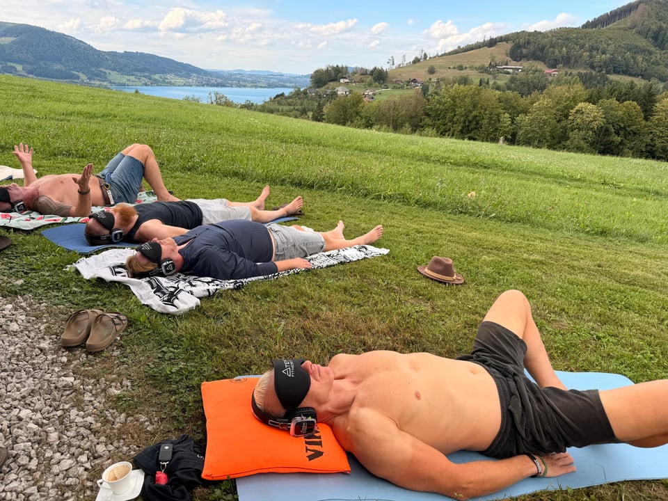 Teilnehmende liegen mit Augenmasken auf der Wiese mit Seeblick
