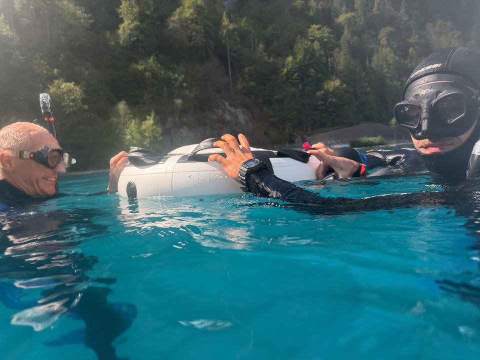 Teilnehmende mit Neoprenanzügen ruhen an einer Boje im Wasser