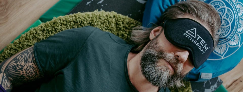Mann liegt mit Atemfitness® Schlafmaske auf einer Matte