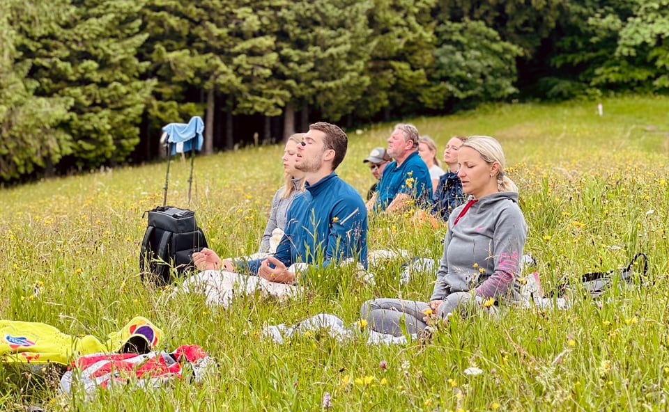 Atemfitness Gruppe sitzt mit geschlossenen Augen auf einer Bergwiese
