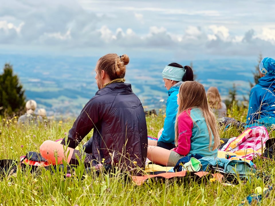 Gruppe meditiert auf einer Bergwiese mit Blick ins Tal