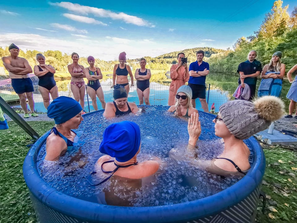 Sechs Teilnehmerinnen sitzen gemeinsam in einem großen Eisbad am See